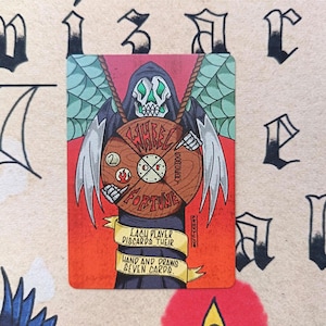 May include: A rectangular game card featuring a skeletal figure with green accents and wings holding a wooden wheel labelled Wheel of Fortune. The card includes a yellow banner with the text Each player discards their hand and draws seven cards.
