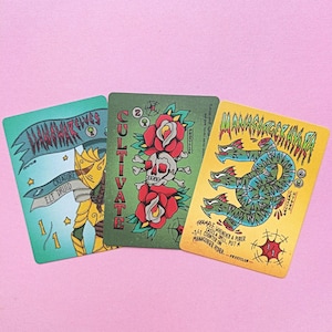 Könnte beinhalten: Drei illustrierte Sammelkarten mit einzigartigen Designs. Eine Karte zeigt einen Totenkopf und Rosen, eine andere ein Wesen und die dritte eine mehrköpfige Schlange. Die Karten haben einen Vintage-Tattoo-Stil mit leuchtenden Farben und Text.