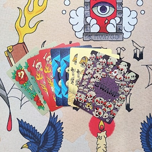 May include: A fan of playing cards featuring diverse graphic illustrations including red roses, flames, skulls, and a spider web design with the text SWAMP. The cards are arranged in a layered arc, showcasing various colors like green, red, blue, and gold.