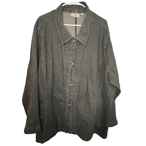 May include: A gray denim button-down shirt with a collar and long sleeves. The shirt features a ruffled placket and is embellished with small, scattered rhinestones. The garment is hanging on a white hanger.