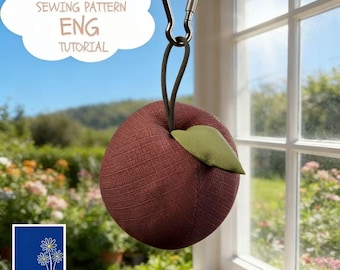 May include: A burgundy-colored, apple-shaped sewing pattern weight with a green leaf, suspended by a black cord and a silver carabiner. The image includes text that reads "PDF SEWING PATTERN ENG TUTORIAL". The background shows a window with a garden view.