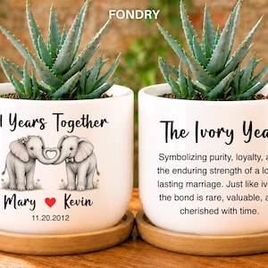 May include: Two white ceramic planters on wooden saucers, each holding an aloe plant. The left planter features two elephants forming a heart with their trunks, the text 14 Years Together, Mary, Kevin, and 11.20.2012. The right planter displays The Ivory Year.
