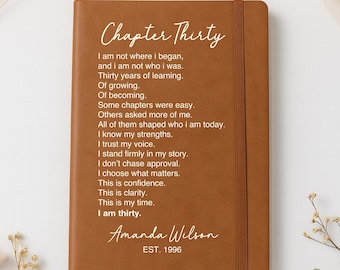 May include: A tan leather-bound journal featuring a vertical elastic closure strap. The cover is printed with the white text Chapter Thirty followed by a poem about personal growth, the name Amanda Wilson, and the text EST. 1996 at the bottom.