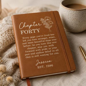 May include: A brown notebook with an elastic closure featuring a white floral line drawing and the text: Chapter FORTY, Every page you've lived has led you here stronger, wiser, and more beautiful than ever before. Jessica EST. 1986.