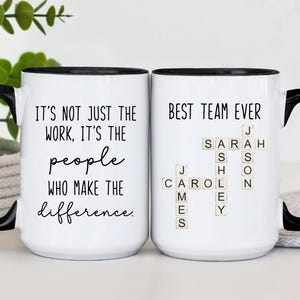 K&ouml;nnte beinhalten: Zwei wei&szlig;e Keramikbecher mit schwarzen Griffen und R&auml;ndern. Auf einem Becher steht "IT'S NOT JUST THE WORK, IT'S THE people WHO MAKE THE difference." Der andere Becher tr&auml;gt die Aufschrift "BEST TEAM EVER" mit Namen, die in Scrabble-Steinen geschrieben sind.
