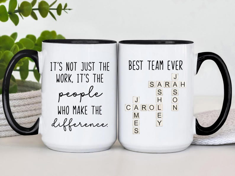 K&ouml;nnte beinhalten: Zwei wei&szlig;e Keramikbecher mit schwarzen Griffen und R&auml;ndern. Auf einem Becher steht "IT'S NOT JUST THE WORK, IT'S THE people WHO MAKE THE difference." Der andere Becher tr&auml;gt die Aufschrift "BEST TEAM EVER" mit Namen, die in Scrabble-Steinen geschrieben sind.