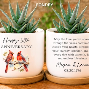 May include: Two white ceramic planters on wooden saucers, each containing an aloe plant. One planter features the text Happy 50th ANNIVERSARY with two red cardinals on a branch. The other displays a sentimental message for Megan & Lance dated 08.20.1976.