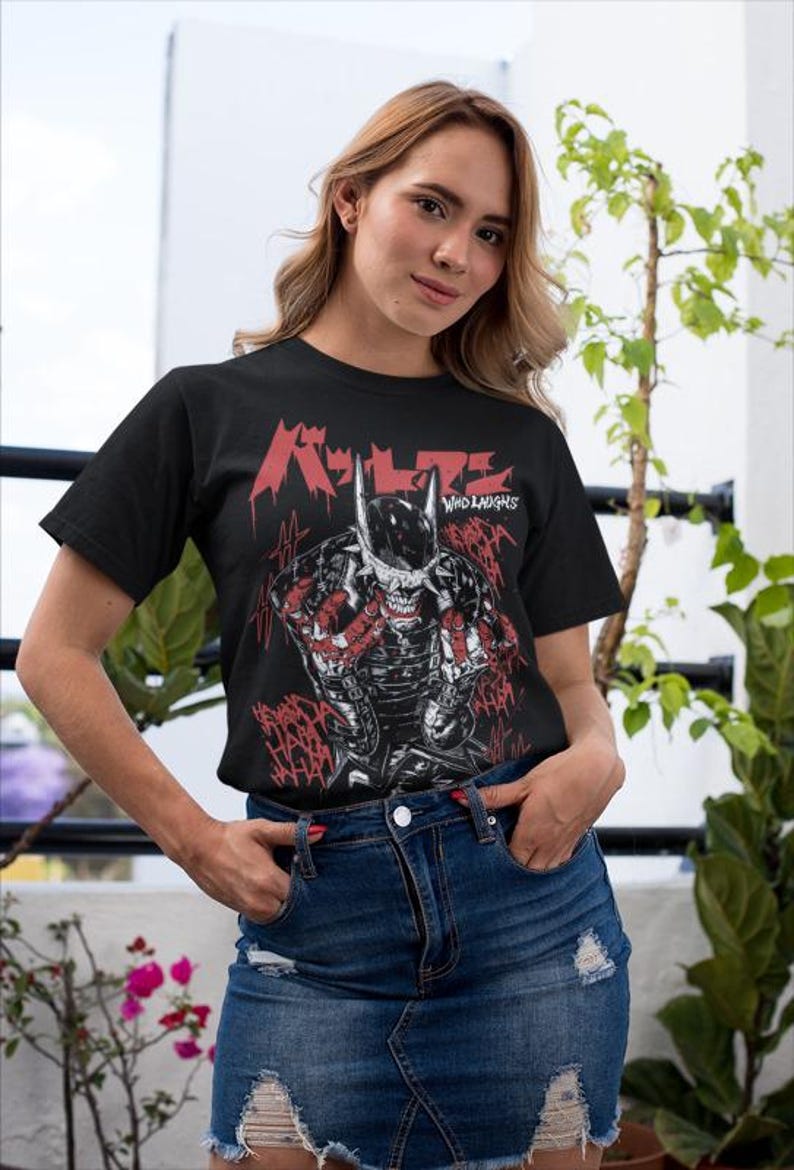 May include: Black t-shirt featuring a graphic of a character with a horned mask and the text "Who Laughs" in red. The design has a comic book style with red accents. The person is wearing a denim skirt.