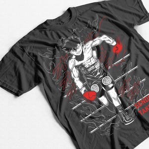 May include: Black t-shirt featuring a dynamic illustration of a boxer in action. The design includes a muscular figure with red boxing gloves, shorts, and the text "SENDA TAKU". White and red graphic elements complete the design.