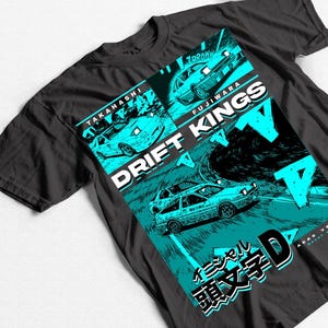 May include: Dark gray t-shirt featuring a teal and white graphic design. The design includes illustrations of cars racing on a track, with the words "DRIFT KINGS" and Japanese text. The shirt has a classic crew neck.