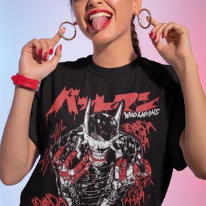 May include: Black t-shirt featuring a graphic of a skeletal figure with a horned helmet and the text "WHO LAUGHS" in white. Red Japanese text is above the graphic. The figure is surrounded by the word "HAHA" in red.
