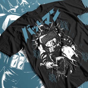 Puede incluir: Camiseta negra con una ilustración en blanco y negro de un guerrero con púas y un martillo. El diseño incluye texto japonés en azul claro, con elementos gráficos azules adicionales.