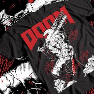 May include: Black t-shirt featuring a detailed illustration of a futuristic warrior with a weapon, rendered in white and red. The word "DOOM" is printed in large red letters across the top. The design includes graphic elements and skulls.