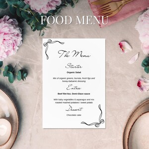 May include: A white menu card with the text "FOOD MENU" and "The Menu" in elegant script. The menu lists an organic salad, beef filet 6oz, and chocolate cake. Floral and decorative elements frame the card, with a background of pink flowers and a marble surface.