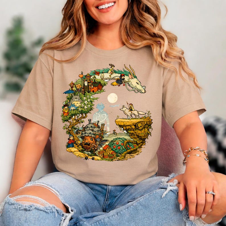 Puede incluir: Camiseta color canela con una colorida ilustraci&oacute;n de un drag&oacute;n, personajes y una luna llena. El dise&ntilde;o gr&aacute;fico incluye una variedad de figuras y edificios animados. La camiseta est&aacute; hecha de un material suave.