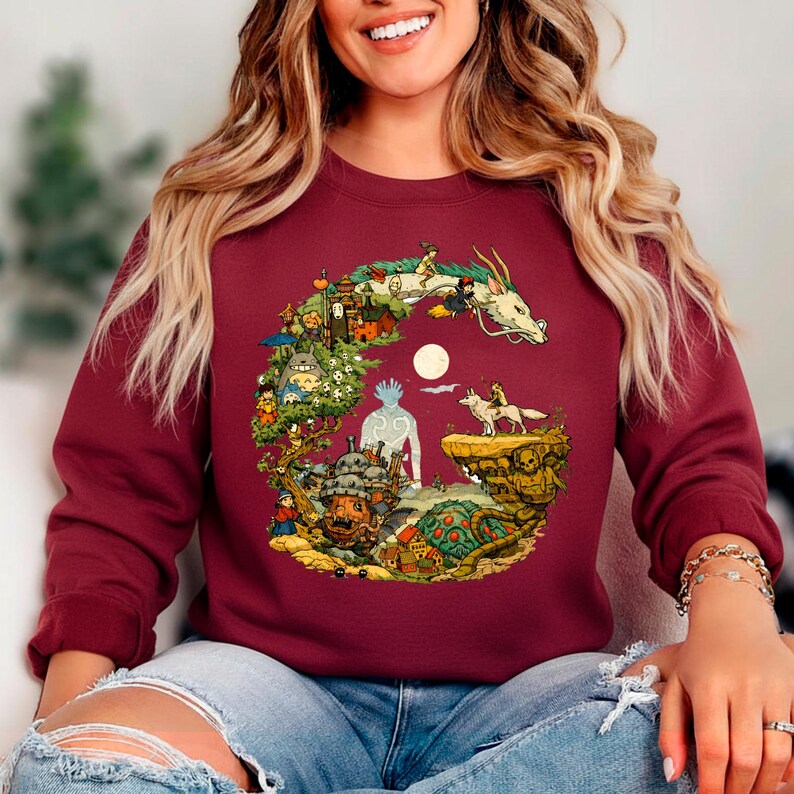 Puede incluir: Sudadera burdeos con una colorida ilustraci&oacute;n de un drag&oacute;n, personajes y paisajes. El dise&ntilde;o tiene la forma de una letra "G". La sudadera est&aacute; hecha de un material suave.