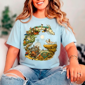 Puede incluir: Camiseta azul claro con una colorida ilustraci&oacute;n de un drag&oacute;n, personajes y un paisaje. El dise&ntilde;o incluye un drag&oacute;n blanco, un lobo y varias figuras animadas. La camiseta est&aacute; hecha de un material suave.