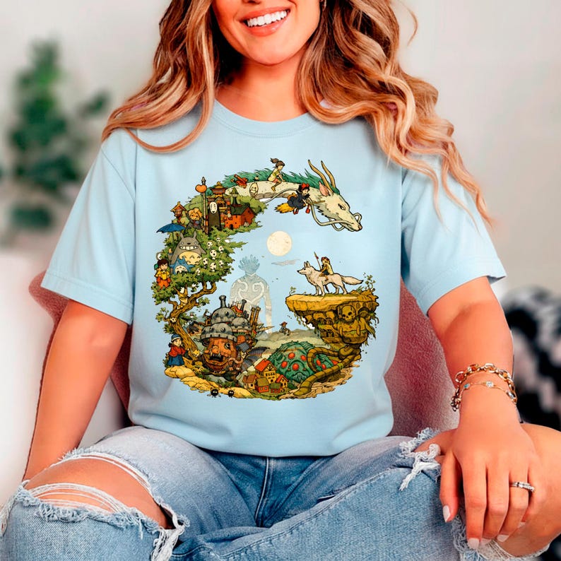 Puede incluir: Camiseta azul claro con una colorida ilustraci&oacute;n de un drag&oacute;n, personajes y un paisaje. El dise&ntilde;o incluye un drag&oacute;n blanco, un lobo y varias figuras animadas. La camiseta est&aacute; hecha de un material suave.