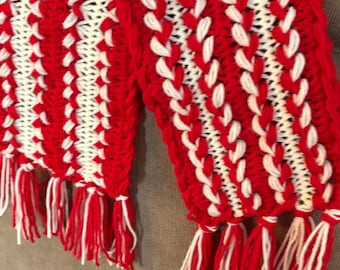 May include: A handmade red and white crochet scarf with a striped pattern. The scarf features alternating vertical stripes of red and white crochet stitches. The ends of the scarf are finished with red and white fringe.