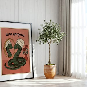 Könnte beinhalten: Gerahmter Kunstdruck mit einer Cartoon-Schlange, die ein Handtuch trägt und in einen Spiegel blickt. Der Druck hat einen pfirsichfarbenen Hintergrund mit den Worten "Hello gorgeous". Eine Vase mit Rosen ist ebenfalls enthalten. Der Druck ist in einem schwarzen Rahmen.
