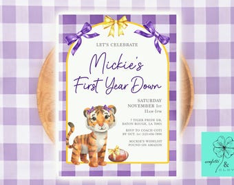 May include: A personalised invitation with a watercolour illustration of a tiger cub, announcing "Mickie's First Year Down." The design features purple and gold accents, with event details. The invitation is set against a purple gingham background.