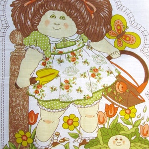 May include: A Cabbage Patch Kid doll with brown hair and a green and white dress is holding a yellow watering can and a green trowel. The doll is standing in a garden with flowers, a cabbage, and a butterfly.