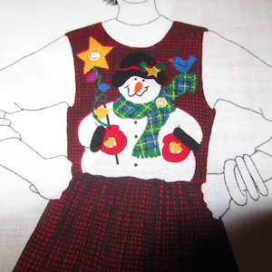 May include: A red and black plaid dress with a white long-sleeved shirt. The dress features a snowman design on the bodice, with a black hat, green scarf, and red mittens. A yellow star and blue bird are also part of the design.