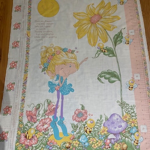 May include: A growth chart featuring a whimsical fairy with blonde hair and a blue dress standing in a garden with a large yellow daisy, mushrooms, and bees. The chart includes a quote about flowers and tiny creatures. "There are flowers and tiny creatures who are happy as can be Sharing sunshine, love and laughter While they're growing merrily."