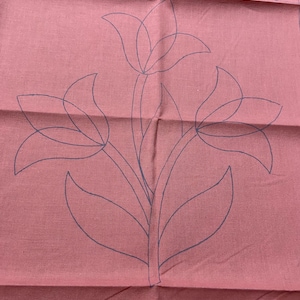 May include: A close-up of a pink fabric with a black outline of three tulips and leaves. The fabric has a diamond pattern border.
