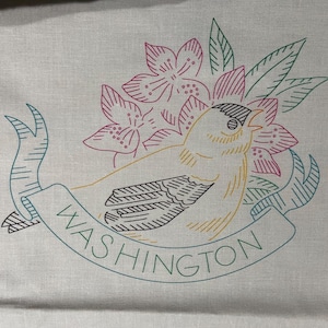 May include: Embroidered design featuring a yellow bird with black wings, surrounded by pink and green flowers. The design is on a white fabric background and includes the word "WASHINGTON" in a green banner.