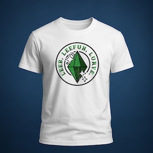 May include: White t-shirt featuring a circular graphic with the text "LEEB, LEEFUH, LURVE" around a green gem design. The graphic includes two stars and a diamond shape. The t-shirt has short sleeves and a crew neck.