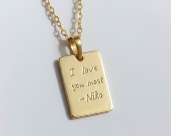 May include: Gold-colored rectangular pendant necklace with the inscription "I love you most - Niko". The pendant hangs from a delicate gold chain. The necklace is displayed against a white background.