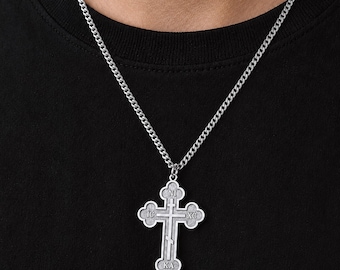 May include: A silver-toned metal cross pendant on a matching curb chain necklace. The cross features a trefoil design at each end and is engraved with the Greek letters IC, XC, NI, and KA arranged around the central vertical and horizontal bars.