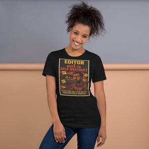 Peut inclure: T-shirt noir avec un graphisme portant l'inscription "EDITOR NOTE TO SELF-DESTRUCT". Le motif comprend une illustration d'une personne devant un ordinateur avec des post-it. La phrase "EVERY TIME THEY LOCK THE CUT ANOTHER NOTE ARRIVES" est également imprimée sur le t-shirt.
