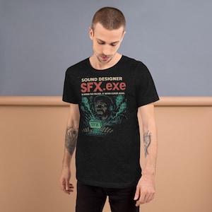 Puede incluir: Camiseta gris oscuro con un diseño gráfico. El texto "SOUND DESIGNER SFX.exe" está sobre una ilustración de una persona con auriculares y usando una laptop, con acentos verdes y azules.