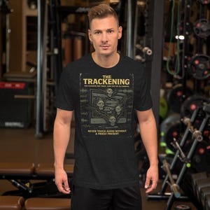 Könnte beinhalten: Dunkelgraues T-Shirt mit einem grafischen Design. Das Design zeigt den Text "THE TRACKENING" und den Satz "YOU CHANGED ONE TRACK, NOW THEY'RE ALL BROKEN." Das Design enthält Schädelmotive und den Text "NEVER TOUCH AUDIO WITHOUT A PRIEST PRESENT."