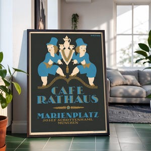 Könnte beinhalten: Ein gerahmtes Poster mit dunkelgrauem Hintergrund, das zwei Figuren in blauen Outfits und Hüten zeigt, die ein zentrales Kaffeeservice halten. Der Text lautet CAFÉ RATHAUS, MARIENPLATZ und JOSEF SCHOTTENHAML MÜNCHEN in blauer und goldener Schrift mit ZIĘTARA oben.