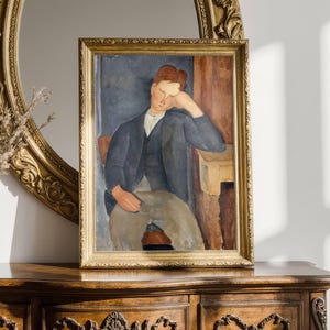 Puede incluir: Pintura enmarcada de una figura sentada con traje oscuro, apoyando la cabeza en la mano. La obra presenta colores apagados y se exhibe en un marco dorado ornamentado. La pintura está sobre una cómoda de madera, con un espejo con marco dorado en el fondo.