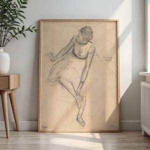 May include: A framed charcoal sketch on beige paper depicting a dancer in a tutu adjusting a slipper. The figure is shown from a high angle, seated with one leg extended. The artwork features visible grid lines and the signature Degas in the corner.