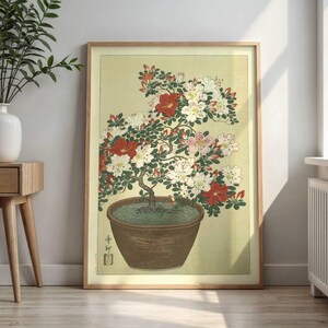Puede incluir: Una lámina enmarcada con una ilustración al estilo de grabado japonés de un bonsái de azalea en maceta. La planta tiene hojas de color verde oscuro y racimos de flores blancas, rosas y rojas en una maceta de cerámica marrón sobre fondo amarillo.
