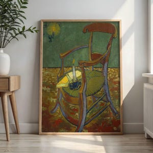 May include: A framed art print depicting a wooden chair with a woven seat, a lit candle, and a book. The painting features a green wall, a yellow floor, and a dark brown chair frame. The artwork is displayed in a light wood frame on a wall.