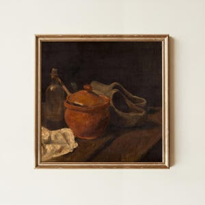 May include: A framed oil painting depicting a still life scene with a dark background. The composition features a terracotta-colored lidded pot, a clear glass bottle, a pair of light-colored wooden clogs, and a crumpled white cloth on a table.