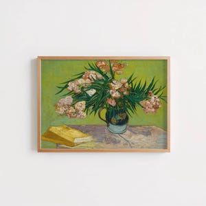 May include: A framed print of a still life painting featuring a bouquet of pink and white flowers in a blue vase. A yellow book rests on a table in front of the vase. The background is a light green color.