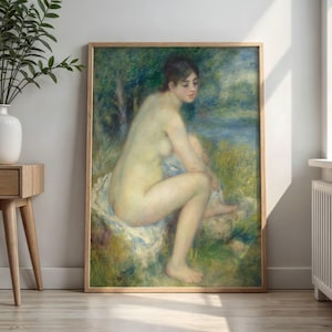 May include: A framed print of a nude woman seated outdoors, rendered in soft, impressionistic brushstrokes. The artwork features a palette of greens, blues, and flesh tones, with a wooden frame. The woman is seated on a white cloth.