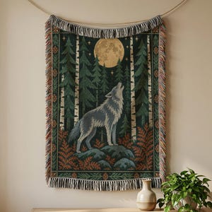 Peut inclure: Un plaid tissé rectangulaire représentant une scène de forêt sombre avec un loup hurlant à la pleine lune. Le motif comprend des pins, des troncs de bouleau et des fougères dans des tons de vert, brun et or, avec des franges décoratives.
