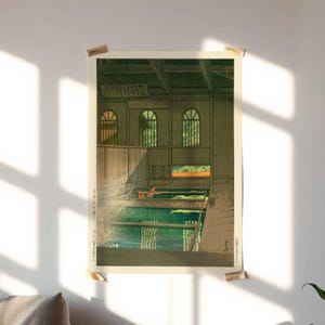 May include: A rectangular art print featuring a woodblock-style illustration of an indoor public bathhouse. The scene depicts a person soaking in a green pool within a wooden structure with arched windows, soft lighting, and traditional Japanese calligraphy.
