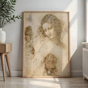 May include: A framed sepia-toned sketch featuring multiple studies of a woman's face and hair. The central figure has long, curly hair and a downward gaze. The artwork is displayed in a light-colored wooden frame, creating a vintage aesthetic.