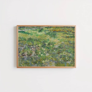 Op de afbeelding: Een rechthoekige ingelijste kunstdruk met een impressionistisch schilderij van een grasveld met zichtbare penseelstreken in tinten groen, geel en bruin. Het kunstwerk is gevat in een lichtgekleurde houten lijst met een strak, eenvoudig profiel.