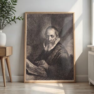 May include: A framed black and white etching print depicting an elderly person with a long beard and a ruff collar, seated at a table with hands clasped over an open book. The artwork features detailed cross-hatching and deep shadows.