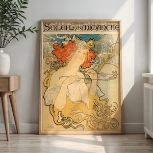 May include: A framed art print featuring the text L'Illustre SOLEIL DU DIMANCHE. The illustration depicts a person with long flowing golden hair, wearing a white garment, adorned with large red flowers and butterflies against a light background.